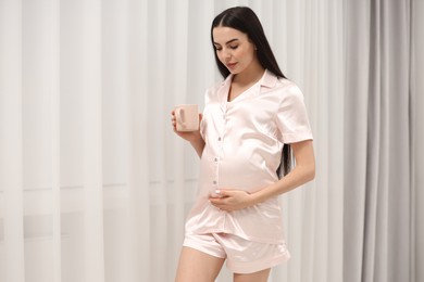 Photo of Pregnant young woman with cup of drink indoors, space for text