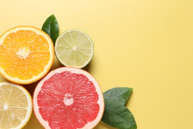 Different cut citrus fruits and leaves on yellow table, flat lay. Space for text