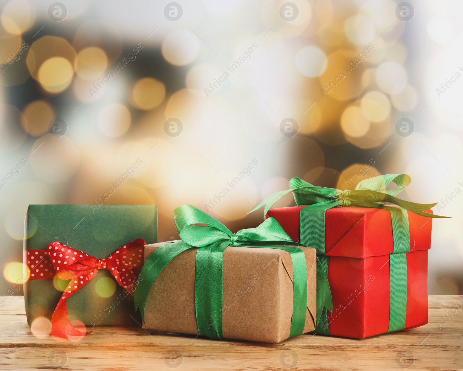 Image of Christmas gift boxes on wooden table against blurred background, bokeh effect