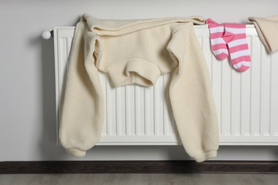 Photo of Teddy sweater, striped socks and hat on heating radiator indoors