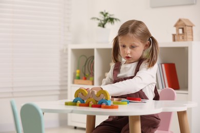 Photo of Cute little girl playing with colorful wooden pieces at white table indoors, space for text. Child's toy