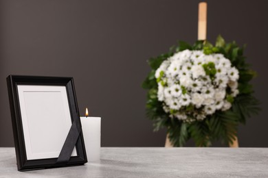 Photo of Photo frame with black ribbon, burning candle on light table and wreath of flowers near grey wall indoors, space for text. Funeral attributes