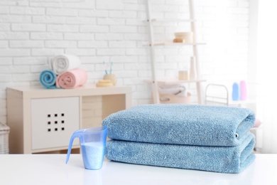 Measuring cup with washing powder and clean towels on table indoors. Laundry day