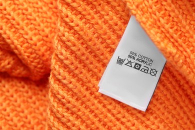 Photo of Clothing label with care recommendations on orange garment, top view. Space for text