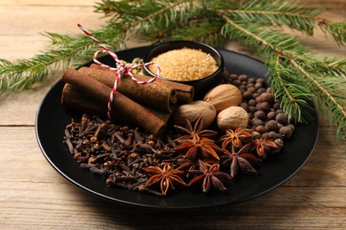 Dishware with different spices and fir branches on wooden table, closeup