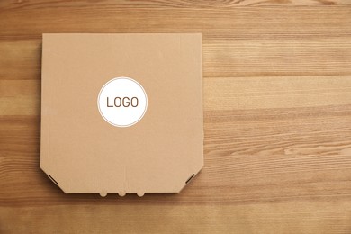 Cardboard pizza box with logo on wooden background, top view. Space for text