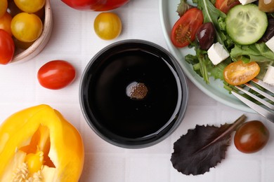 Vinegar in glass, salad and products on white tiled table, flat lay