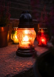 Photo of Different grave lanterns with burning candles on stone surface at night