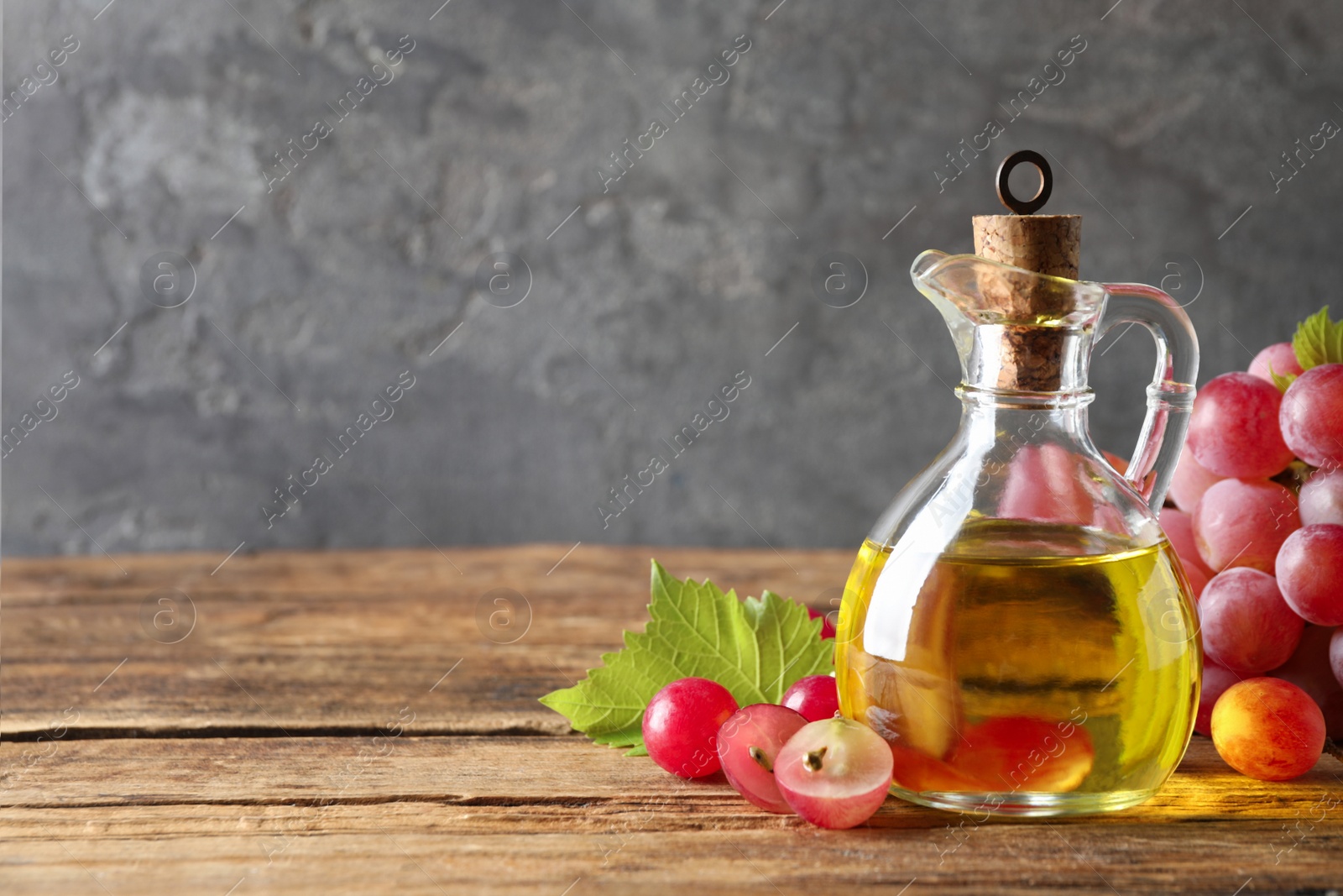 Photo of Jug of natural grape seed oil on wooden table, space for text. Organic cosmetic