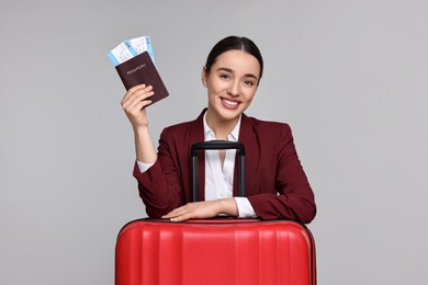 Happy businesswoman with passport, tickets and suitcase on grey background