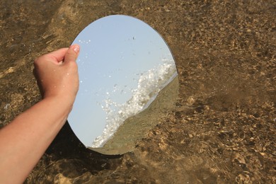 Woman reflecting sea and sky with round mirror on beach, closeup