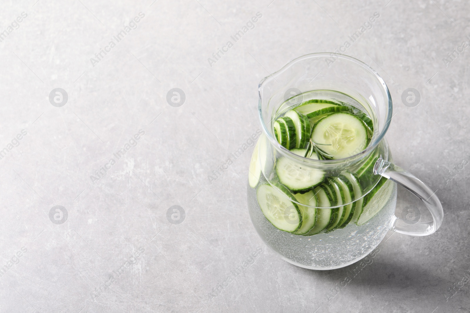 Photo of Jug of fresh cucumber water on grey background. Space for text