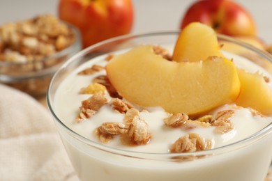 Photo of Tasty peach yogurt with granola and pieces of fruit in dessert bowl on table, closeup