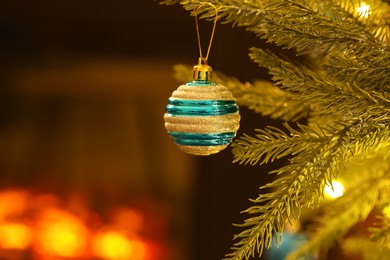 Photo of Beautiful golden Christmas ball hanging on fir tree branch against blurred background, closeup