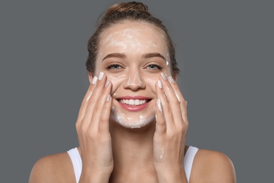 Photo of Young woman washing face with soap on grey background