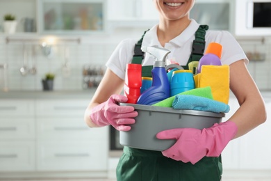 Photo of Woman with basin of detergents in kitchen, closeup. Cleaning service