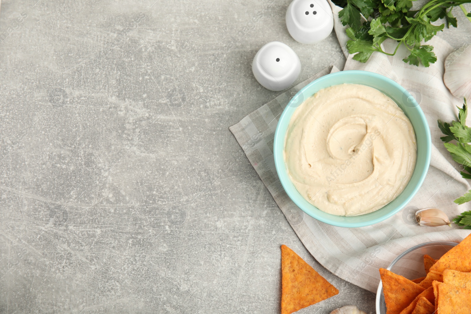 Photo of Delicious hummus, nachos and parsley on grey table, flat lay. Space for text