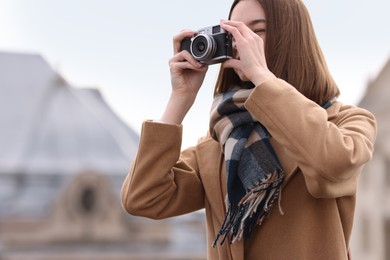 Photo of Beautiful woman in warm scarf taking picture with vintage camera outdoors, space for text