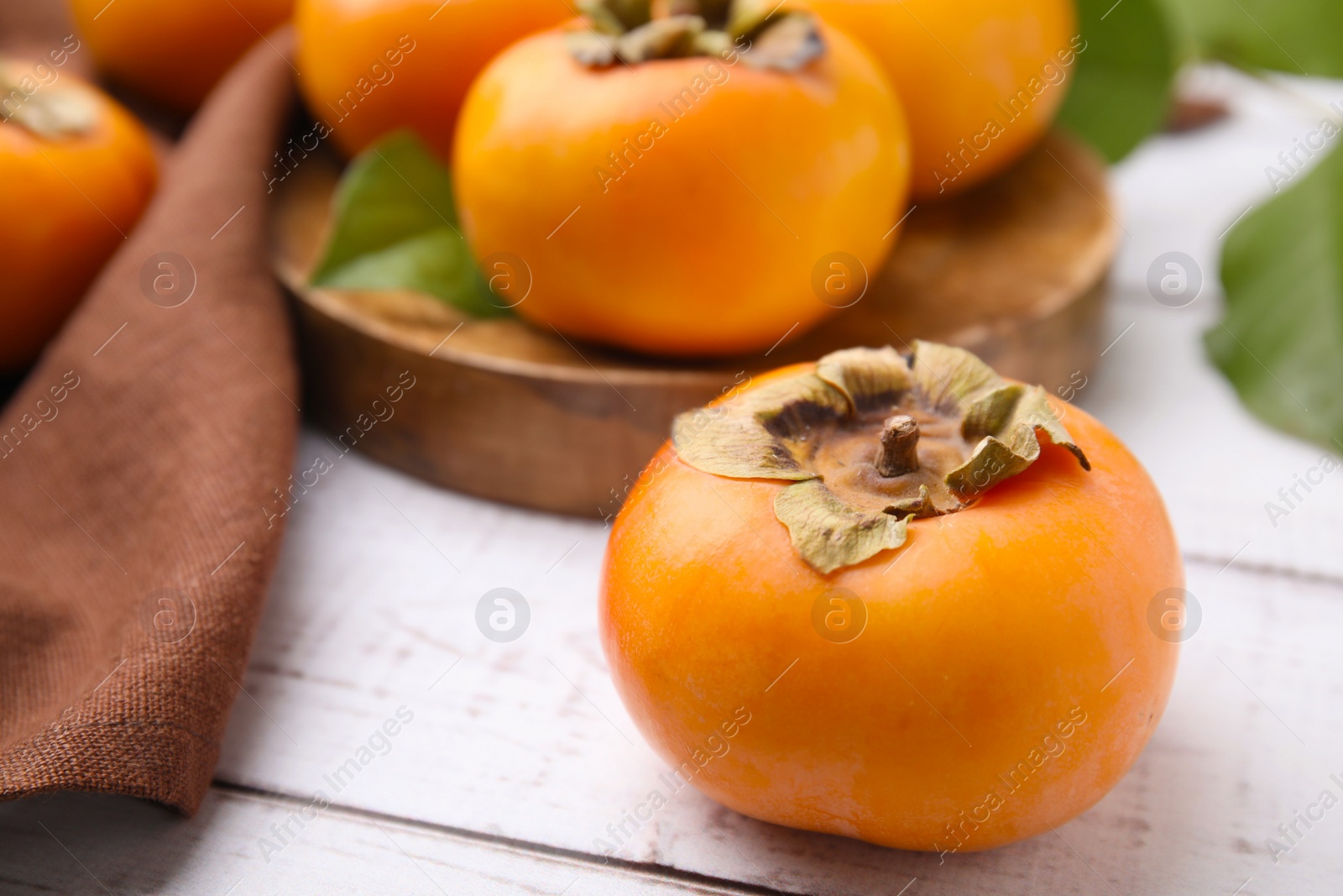 Photo of Delicious ripe juicy persimmons on white wooden table, closeup