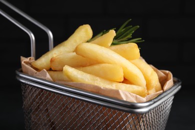 Photo of Frying basket with tasty french fries on dark background, closeup