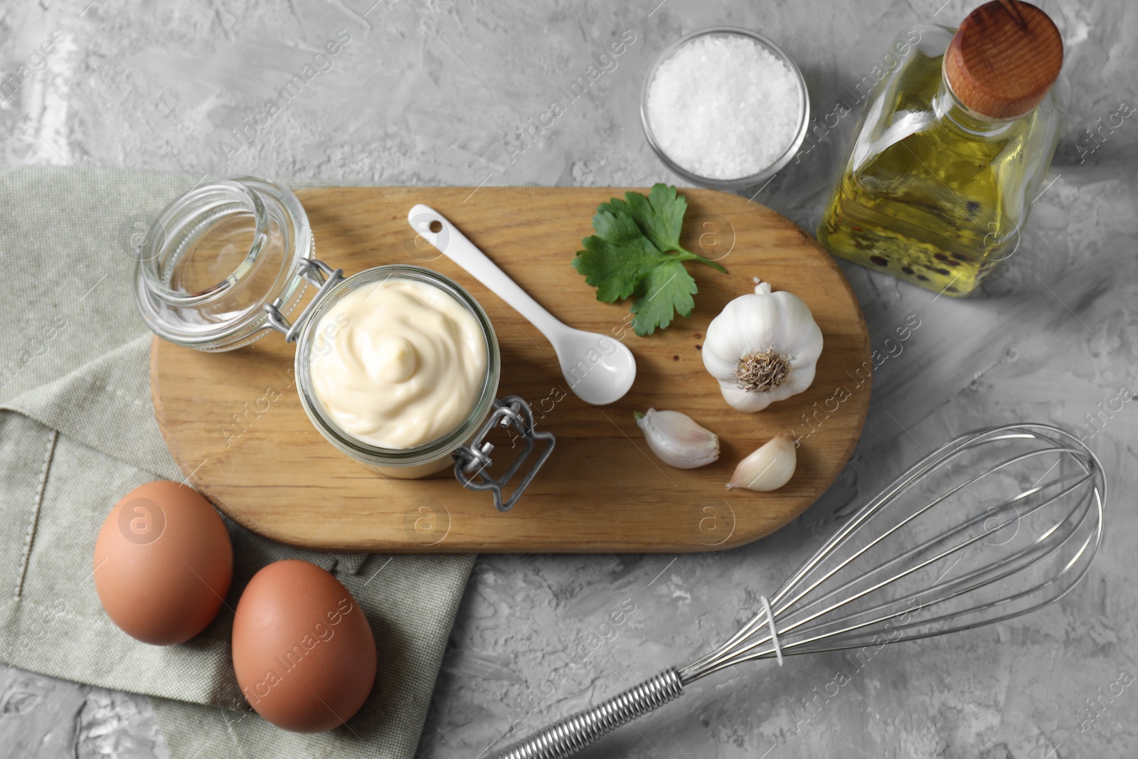 Photo of Tasty mayonnaise in jar, ingredients and whisk on gray textured table, flat lay