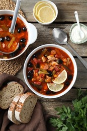 Photo of Meat solyanka soup with sausages, olives and vegetables served on wooden table, flat lay