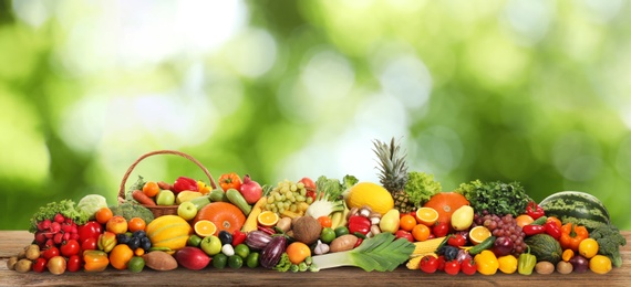 Image of Assortment of fresh organic vegetables and fruits on wooden table against blurred green background. Banner design 