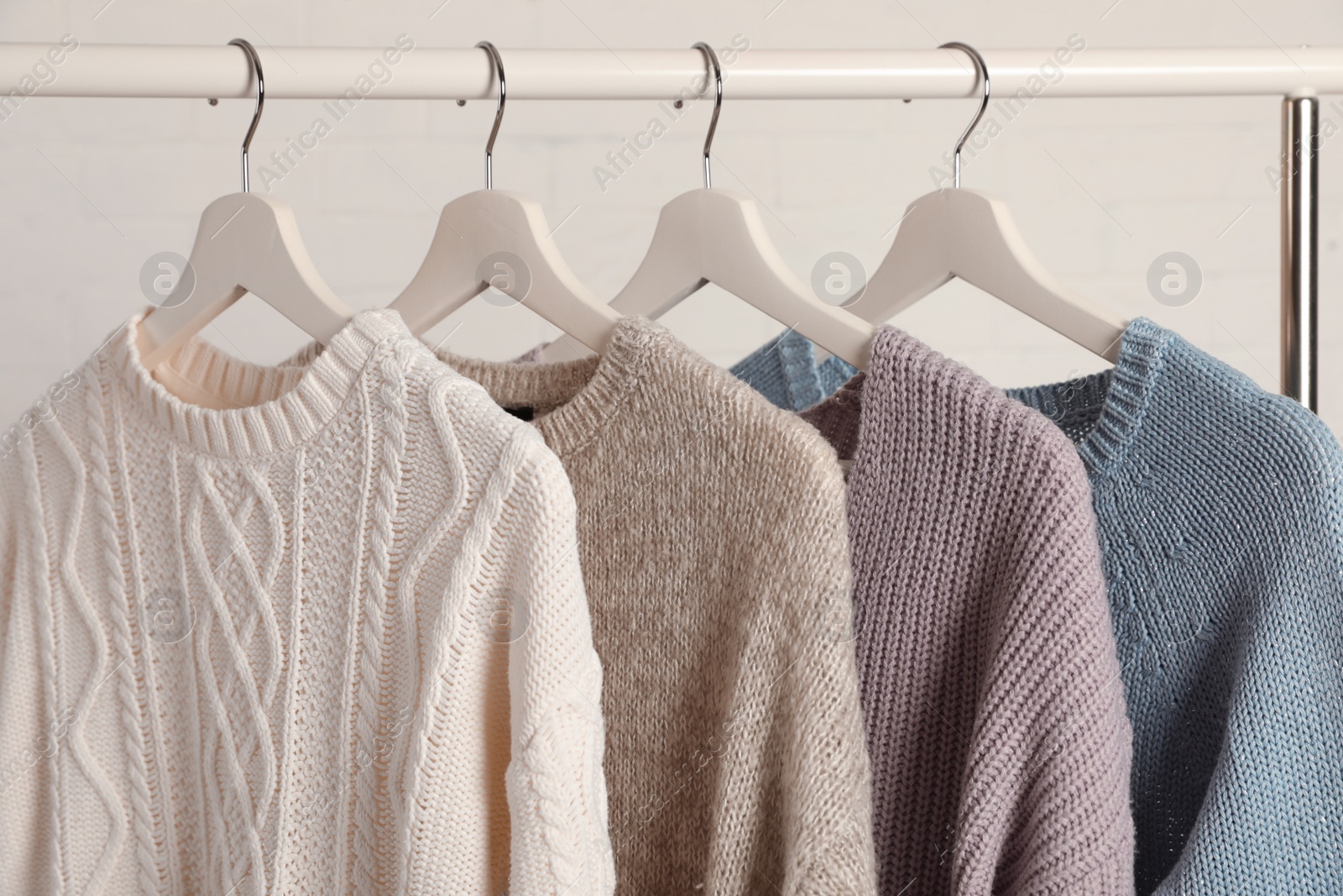 Photo of Collection of warm sweaters hanging on rack against white background, closeup