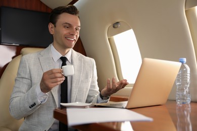 Photo of Businessman with cup of coffee working on laptop at table in airplane during flight