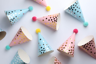 Colorful party hats with pompoms on light background, top view