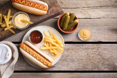 Flat lay composition with delicious hot dogs and French fries on wooden table. Space for text