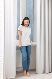 Photo of Young woman in stylish jeans near window indoors