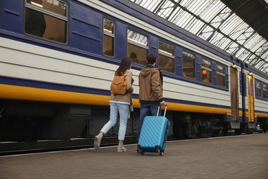 Photo of Being late. Couple with suitcase running towards train at station, back view