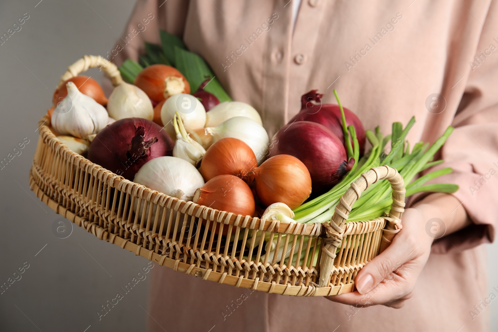 Photo of Woman holding tray with fresh onions and garlic on light background, closeup