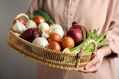 Woman holding tray with fresh onions and garlic on light background, closeup