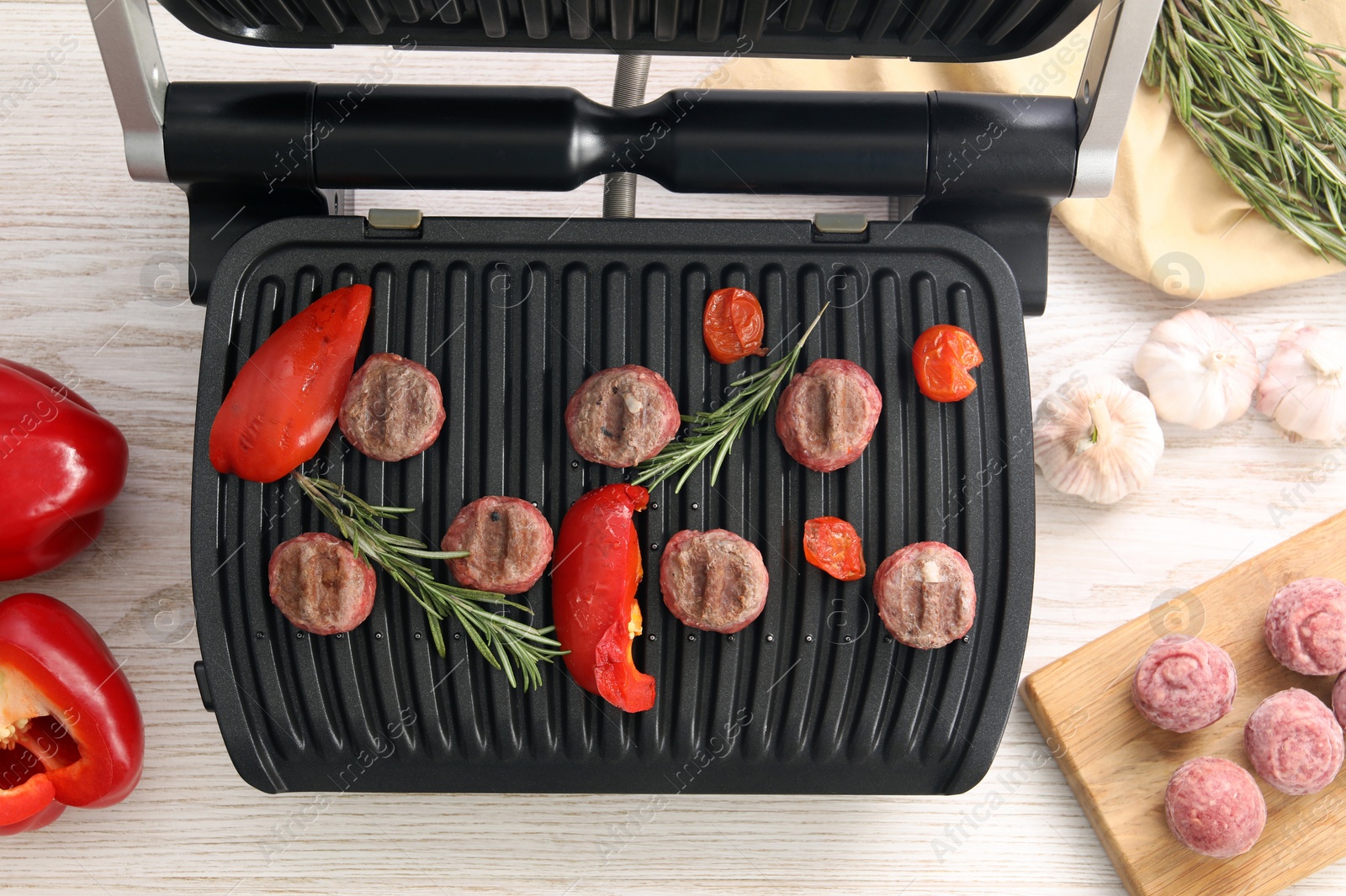 Photo of Electric grill with vegetables, meat balls and rosemary on wooden table, flat lay