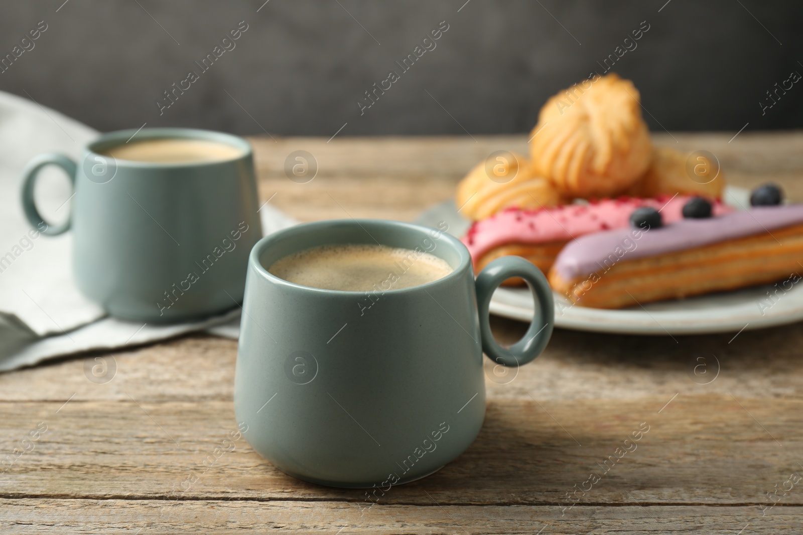 Photo of Aromatic coffee in cups, tasty eclairs and profiteroles on wooden table