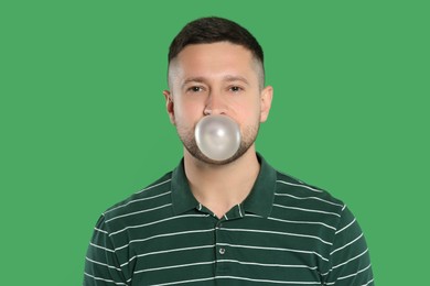 Photo of Handsome man blowing bubble gum on green background