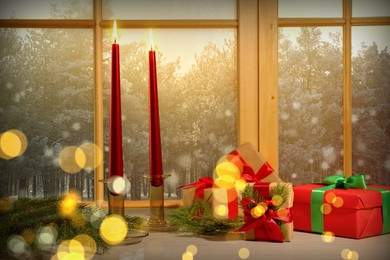 Image of Burning candles, gift boxes and fir branches on window sill indoors. Christmas eve