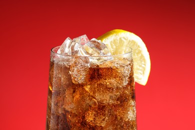 Photo of Glass of refreshing soda drink with ice cubes and lemon on red background, closeup