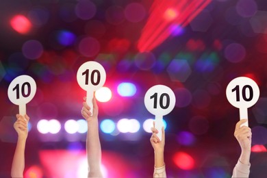 Panel of judges holding signs with highest score against blurred background, closeup. Bokeh effect