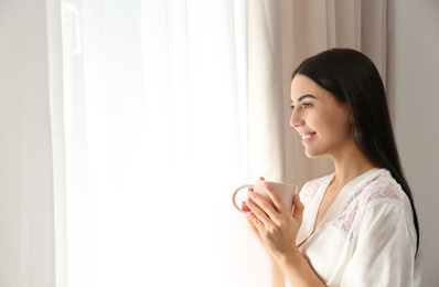 Photo of Young woman with cup of coffee near window. Lazy morning