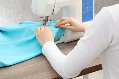 Photo of Seamstress working with sewing machine at wooden table indoors, closeup