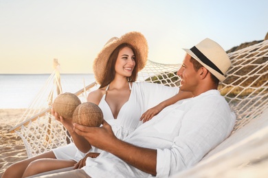 Photo of Happy couple with tropical cocktails relaxing in hammock on beach