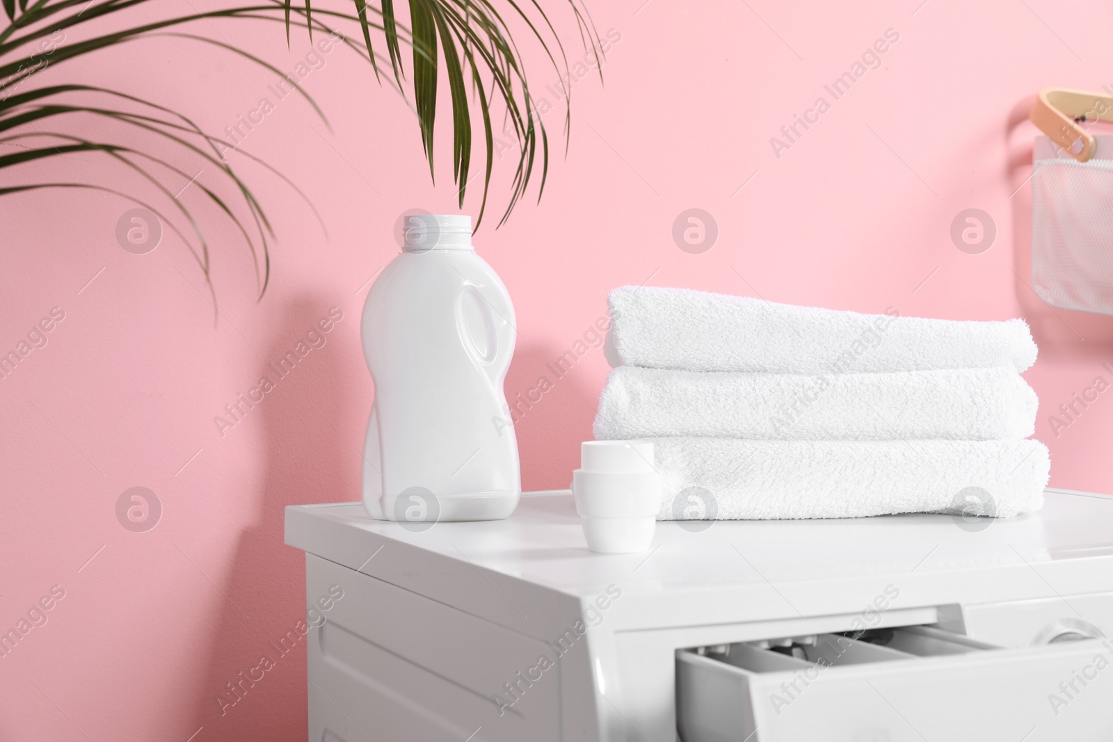 Photo of Bottle with detergent and clean towels on washing machine in laundry room