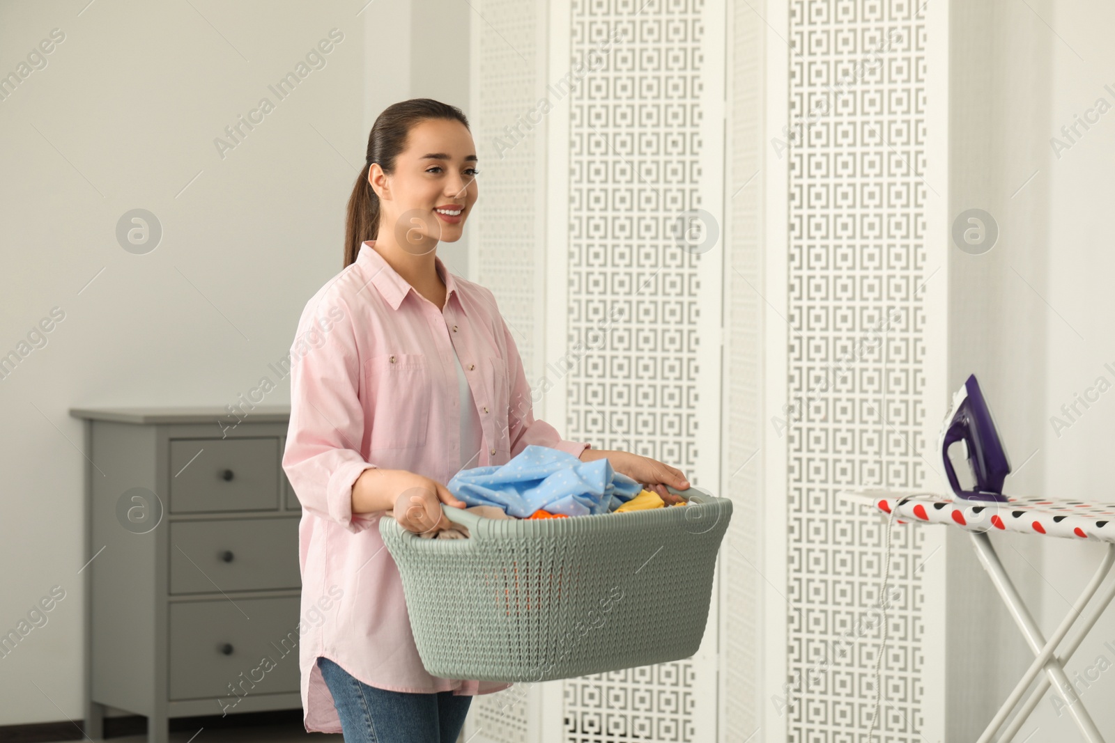 Photo of Young woman with basket full of clean laundry indoors