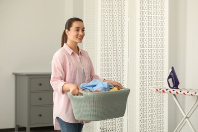 Photo of Young woman with basket full of clean laundry indoors