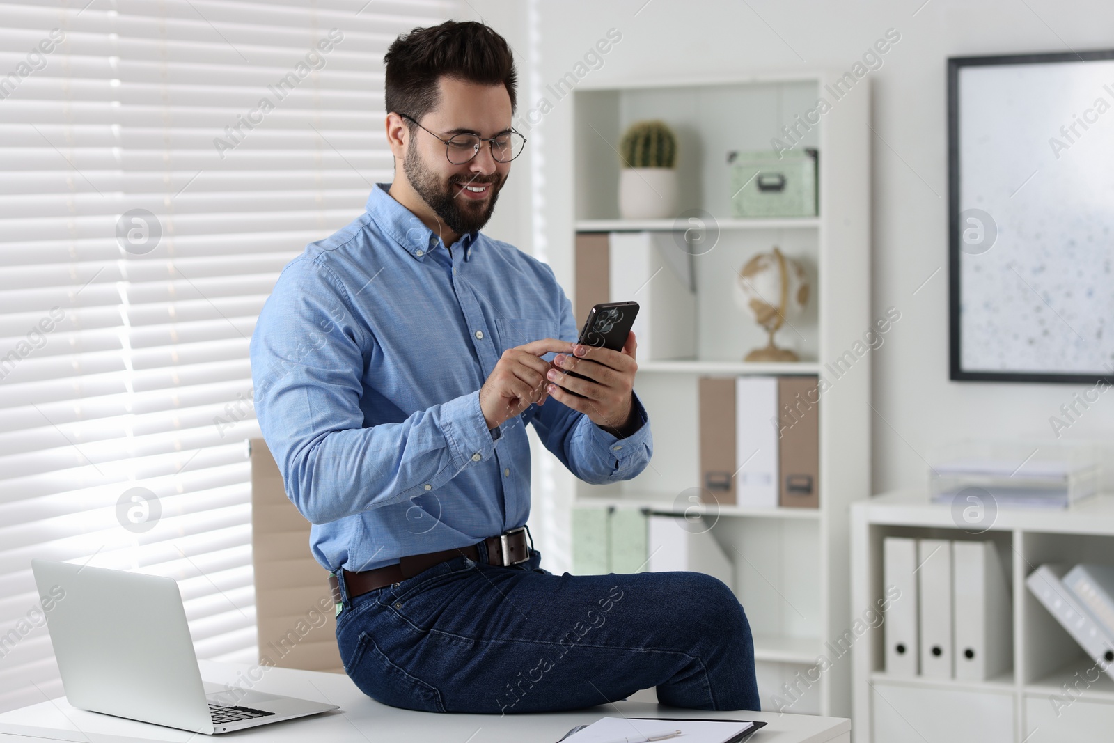 Photo of Happy young man using smartphone in office