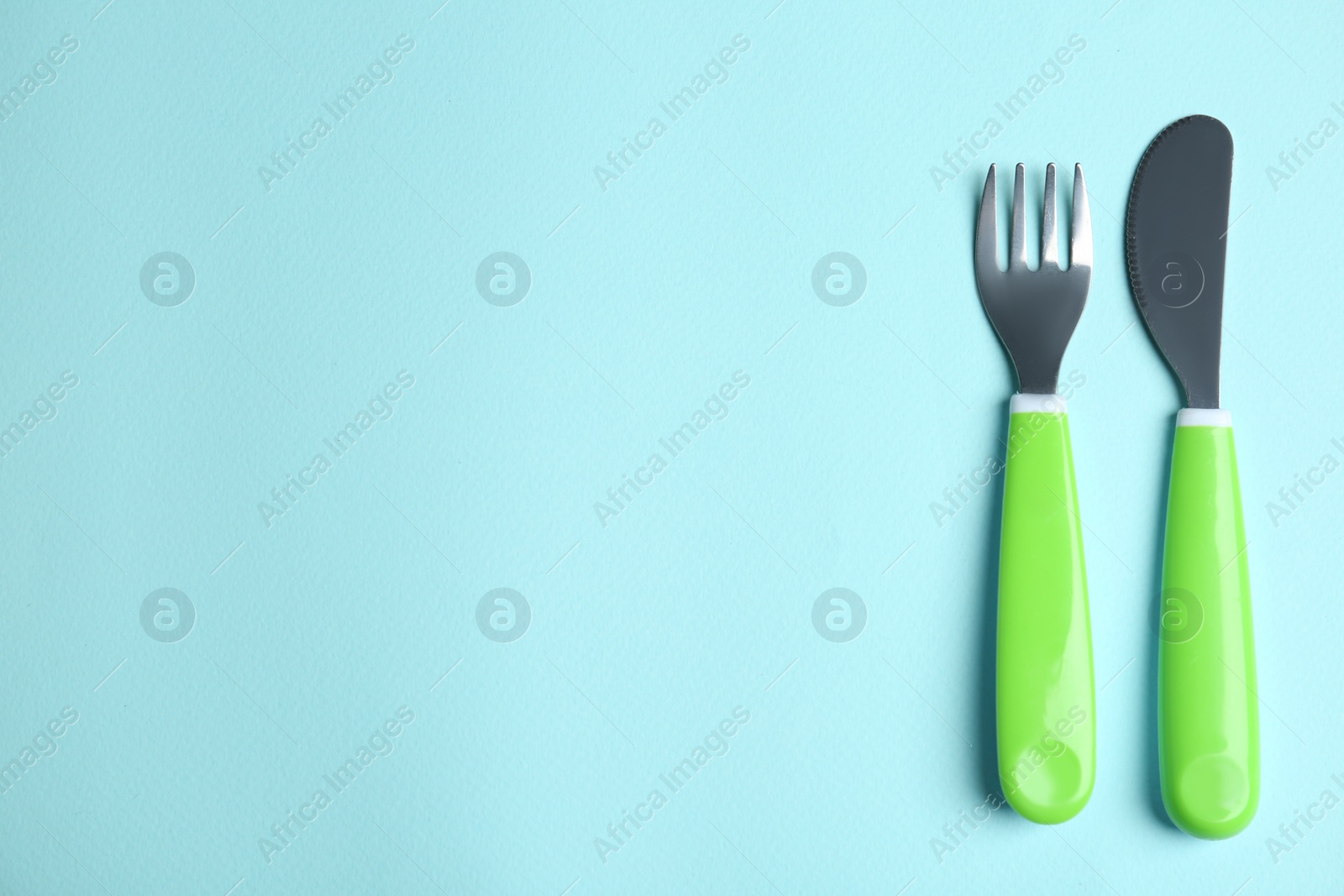 Photo of Small fork and knife on light blue background, flat lay with space for text. Serving baby food