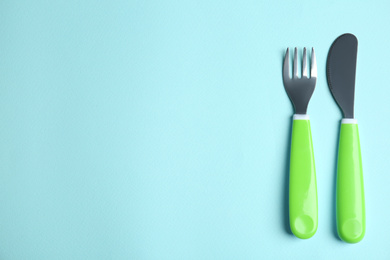 Small fork and knife on light blue background, flat lay with space for text. Serving baby food